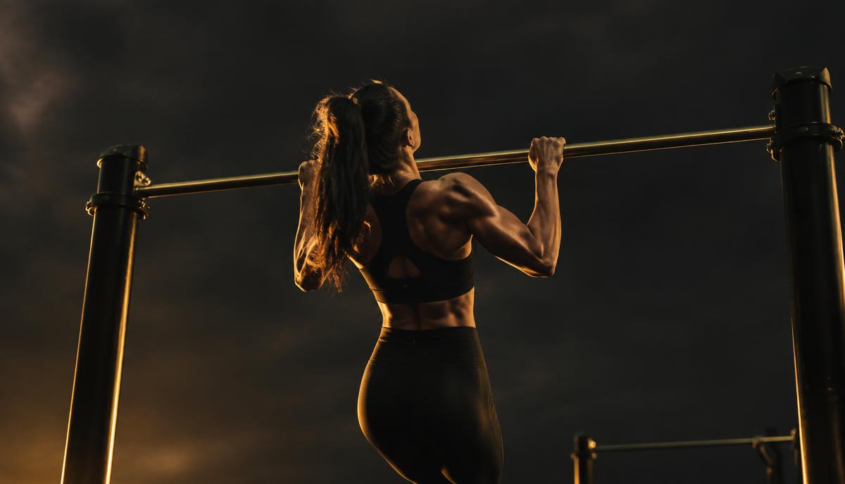 Kvinde tager en strikt pull-up i en calisthenics-park i mørke, gyldne toner